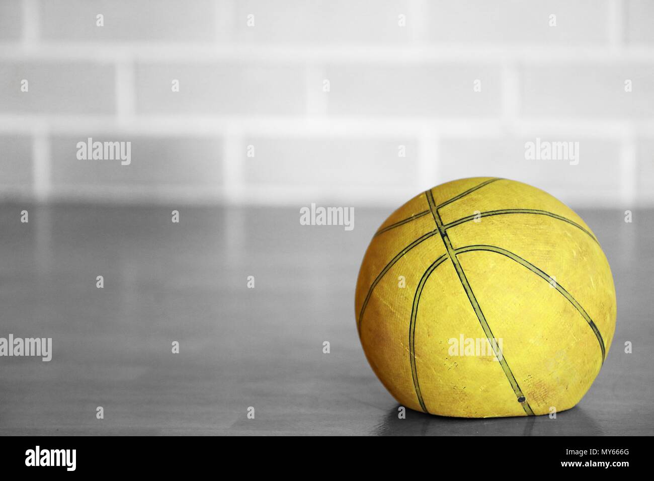 Close up black and white isolated colour color old tired let down deflated worn out spent basketball on a wooden court with blurred brick background.  Stock Photo