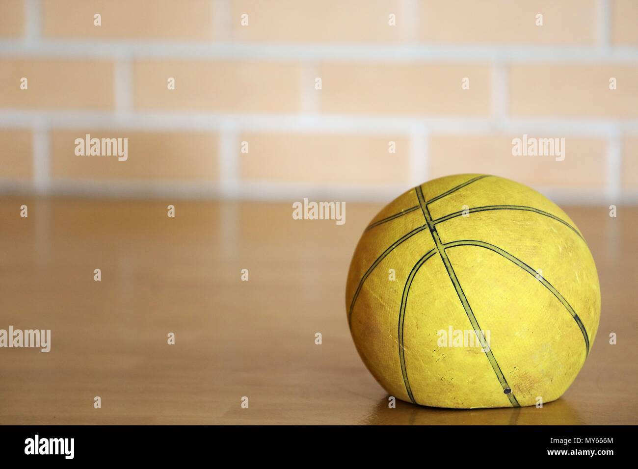 Close up old tired let down deflated worn out spent basketball on a wooden court with blurred brick background. Used sporting equipment, broken, flat, Stock Photo