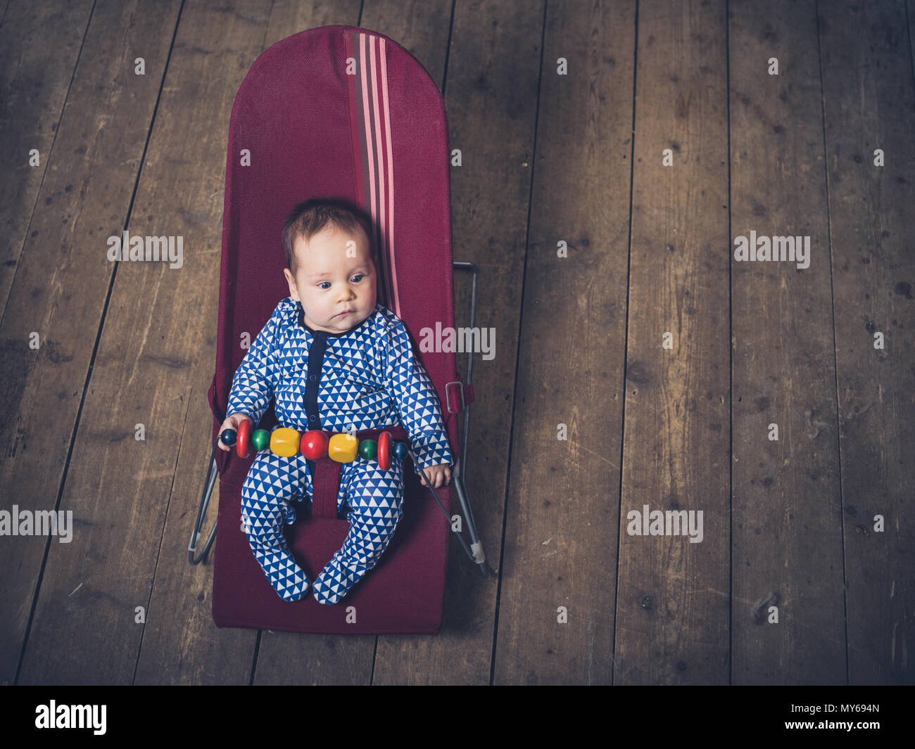 A baby is sitting in a vintage bouncy chair on the wooden floor Stock