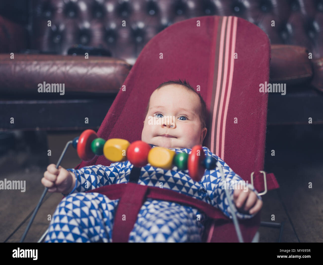 A baby is sitting in a vintage bouncy chair on the wooden floor Stock