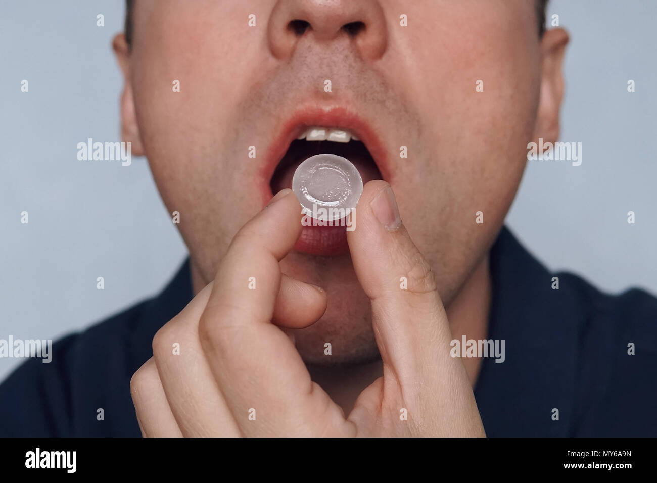 young man puts in his mouth a sucking pill for sore throat. Self-medication for flu and cold. Sick with a sore throat, mint for fresh breath. close up Stock Photo