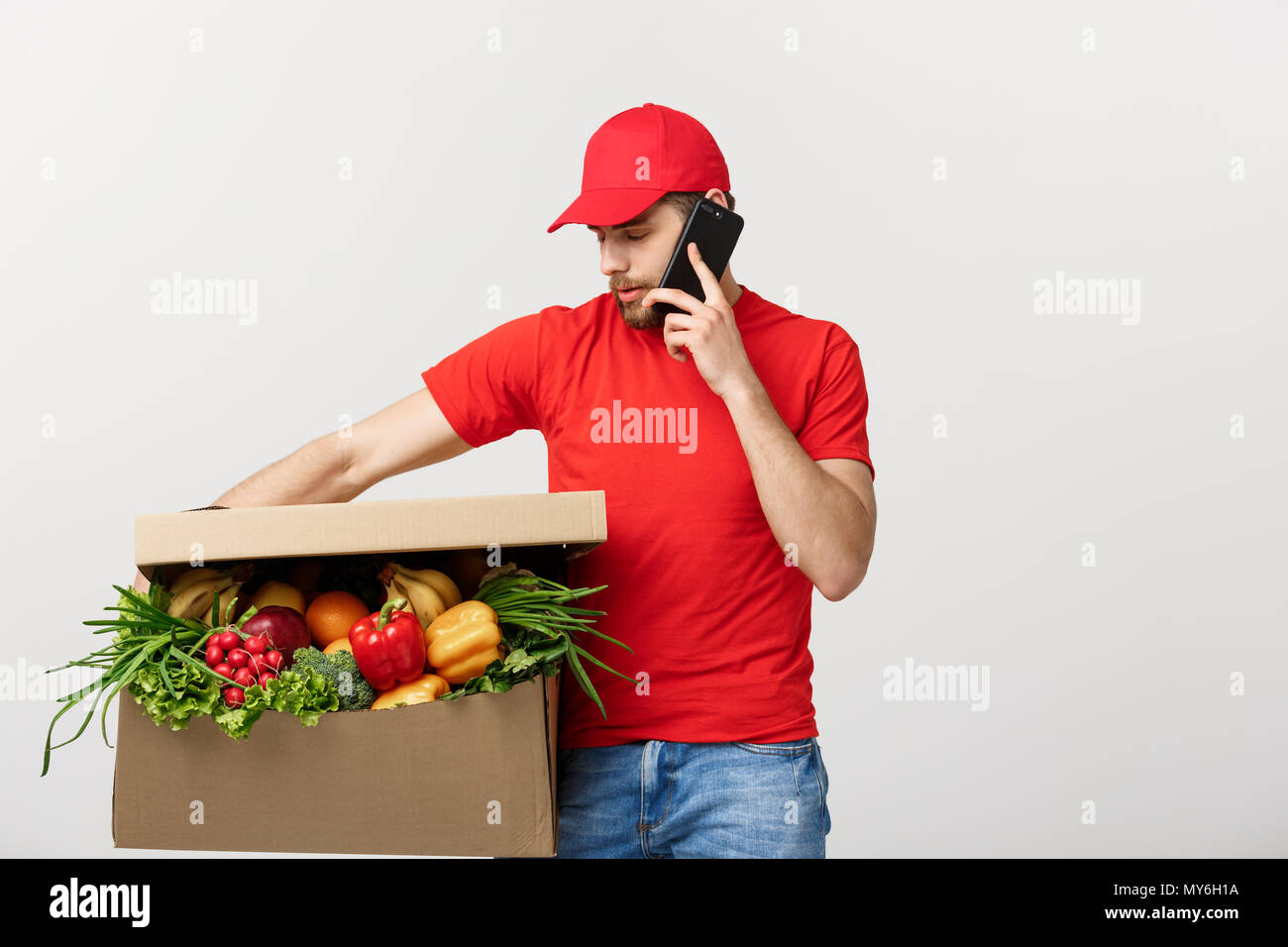 Delivery man holding paper box with food and making a call with mobile