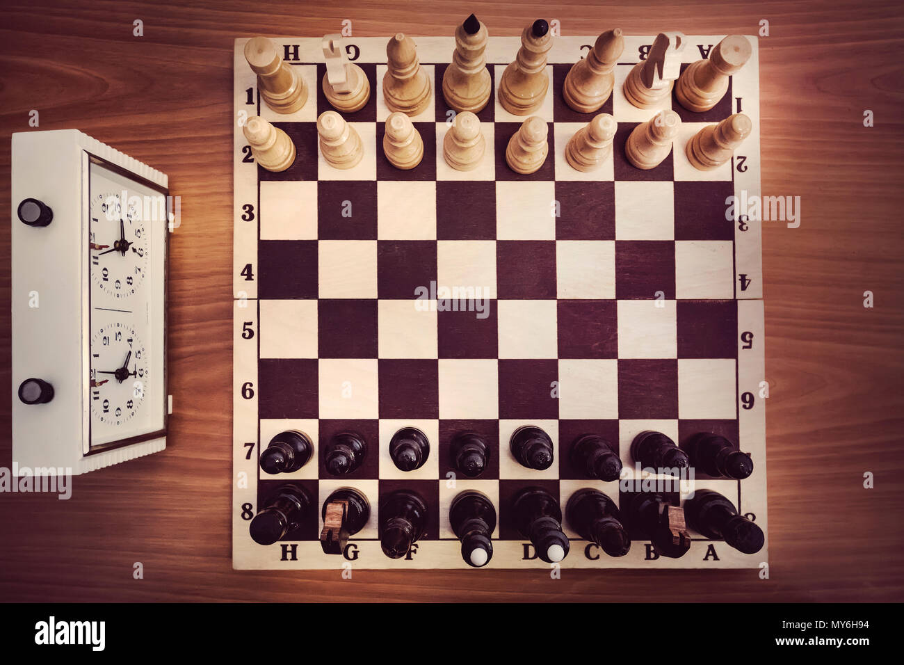 Chessboard with chess and clock, top view. The beginning of the chess