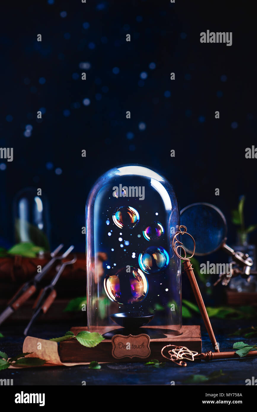Soap bubbles under a glass dome with a DIY bubble wand. Preserving fleeting summer and childhood concept with copy space on a dark background Stock Photo