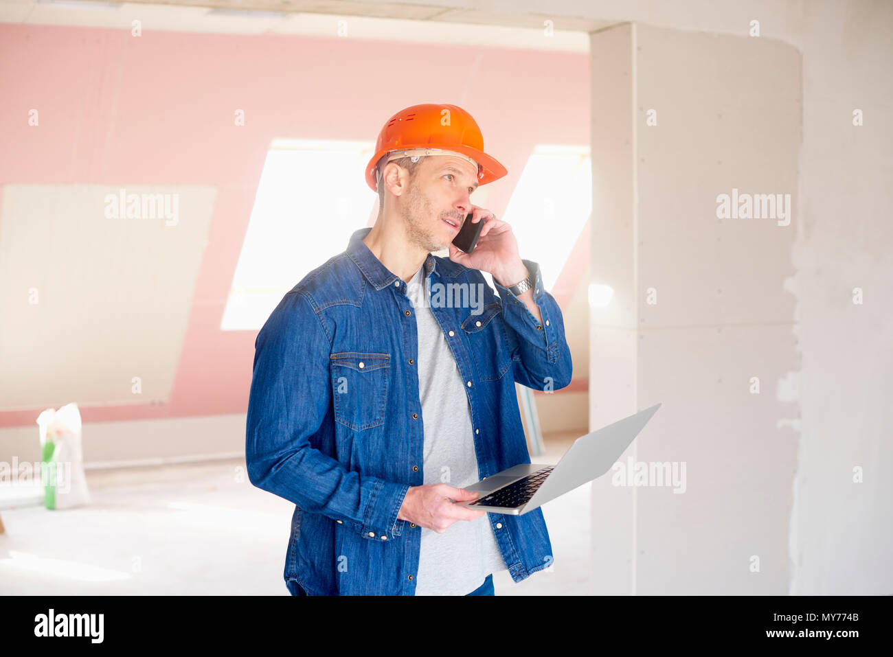 Construction man making call and using his laptop while standing at construction site. Stock Photo