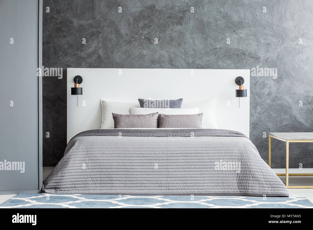 Grey bedsheets on bed with white bedhead against concrete wall in