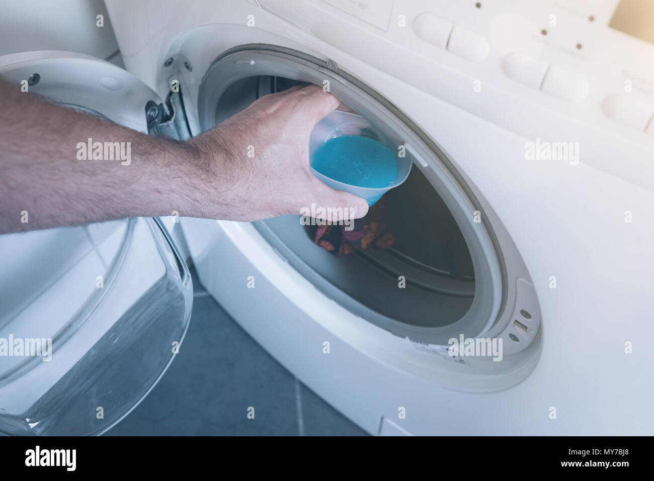 hand placing measuring cap with laundry detergent in washer Stock Photo