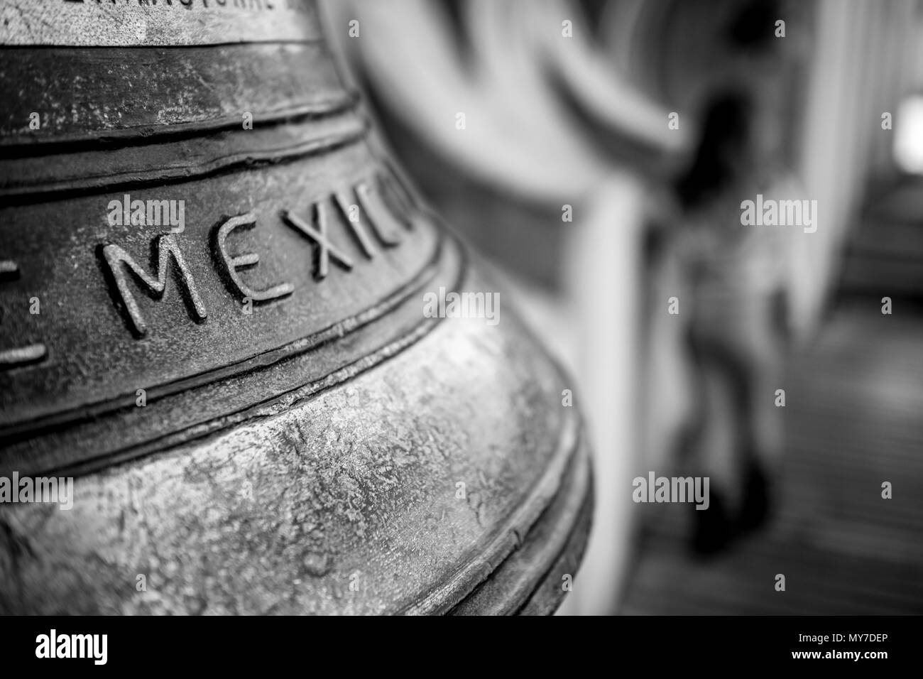 Letter M shallow focus on huge brass bell with caption Mexico with blurred child silhouette in the background in black and white Stock Photo