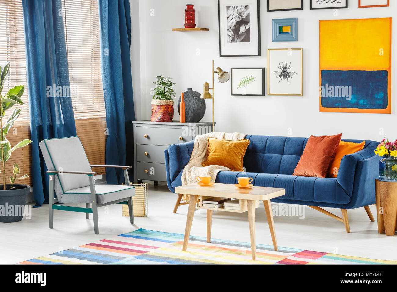 Bright and cozy living room interior with blue drapes, a sofa with orange  cushions, gray armchair and a wooden table with two cups of coffee. Real  pho Stock Photo - Alamy