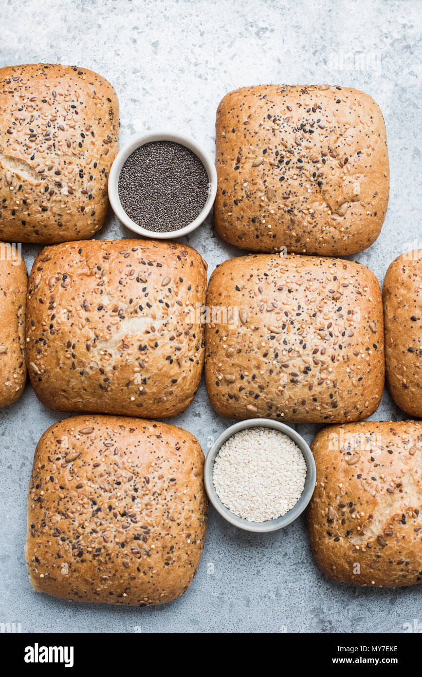 Multigrain bread rolls and bowls of seeds, overhead view Stock Photo