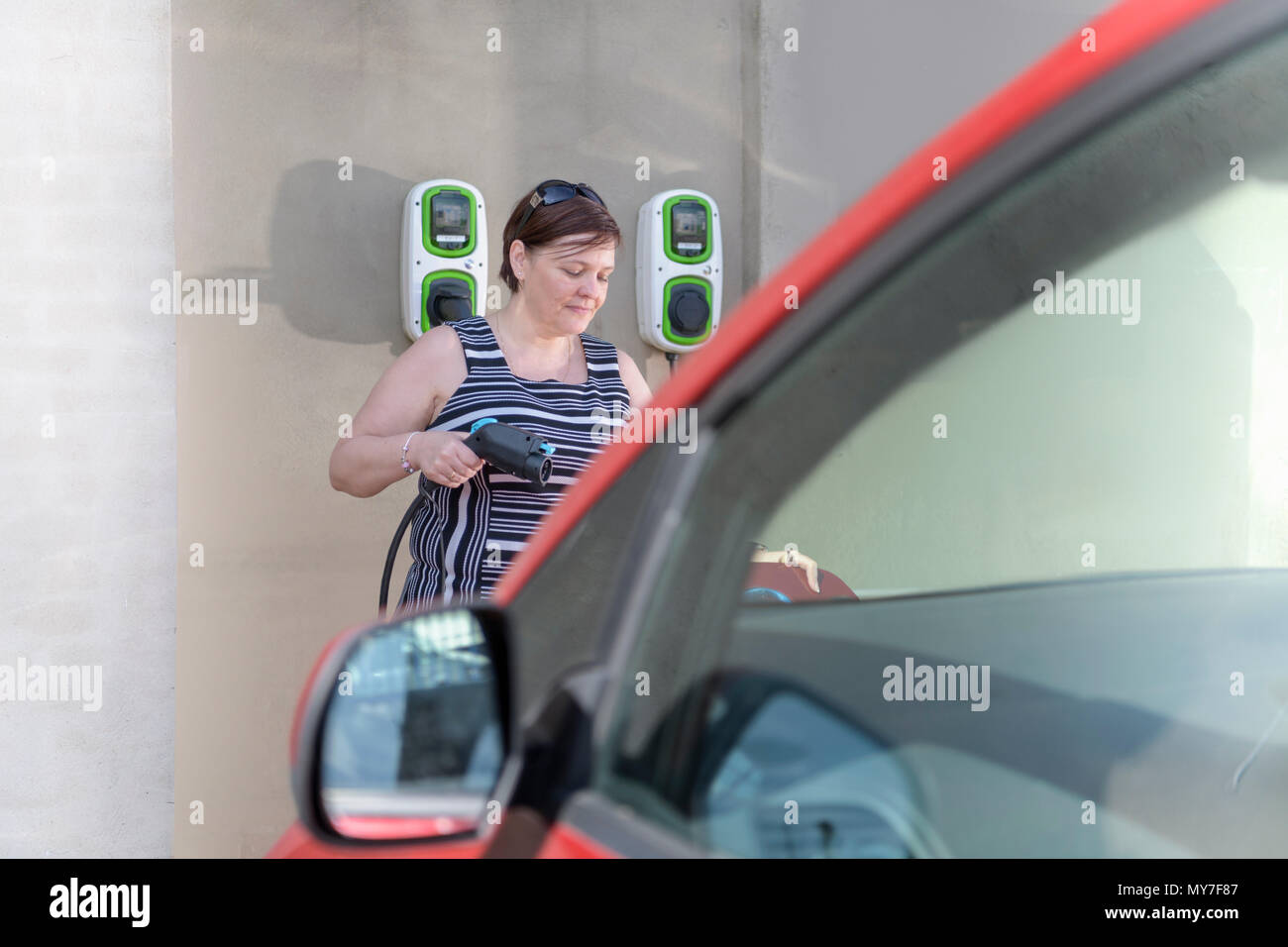 Woman charging electric car at city charging point Stock Photo