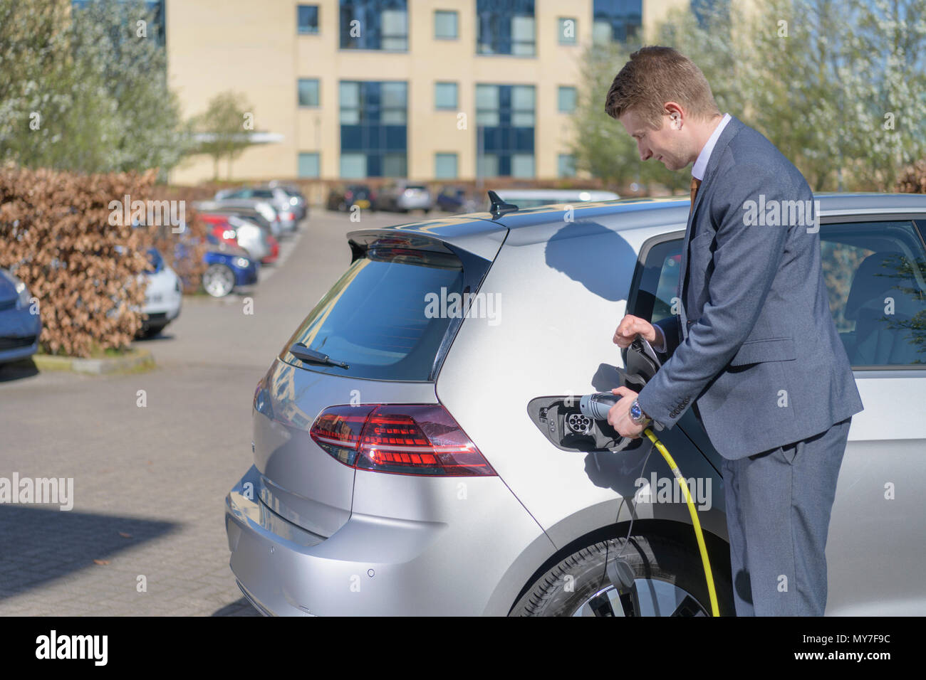Businessman charging electric car at charging point in business park Stock Photo
