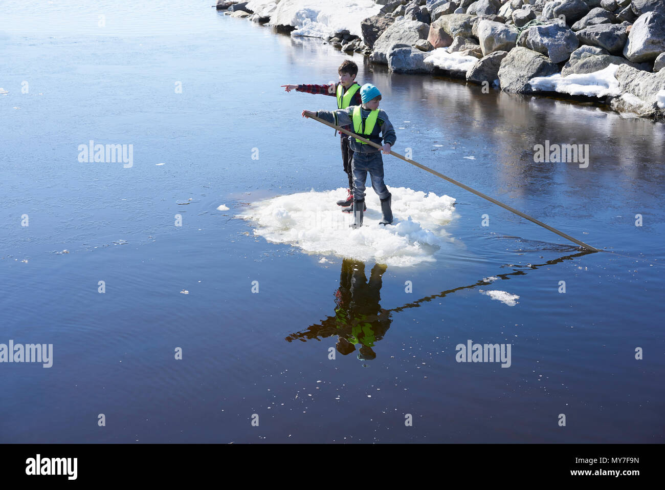 Two boys standing on ice, on lake, pushing themselves along with pole Stock Photo