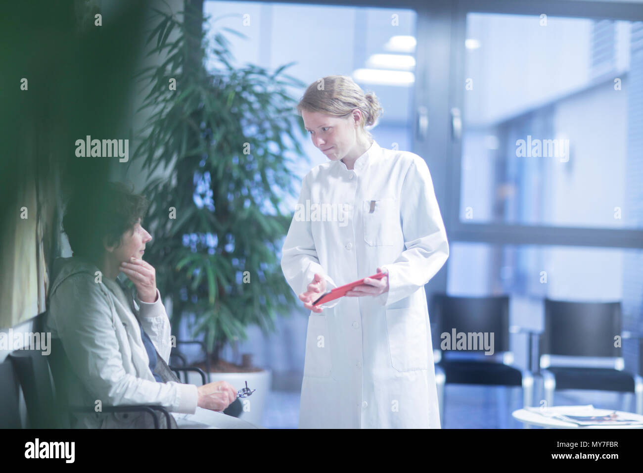 Radiologist, holding digital tablet, talking to mature woman in waiting area of hospital Stock Photo