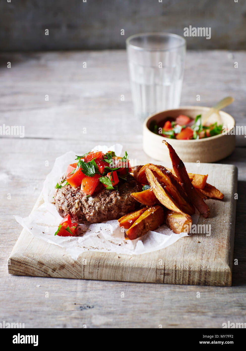 Still life of burger and chips on chopping board with salsa Stock Photo