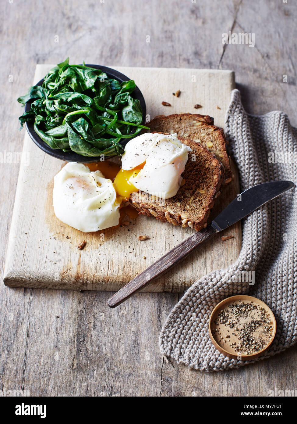 Still life with spinach and poached egg on toast on chopping board, overhead view Stock Photo