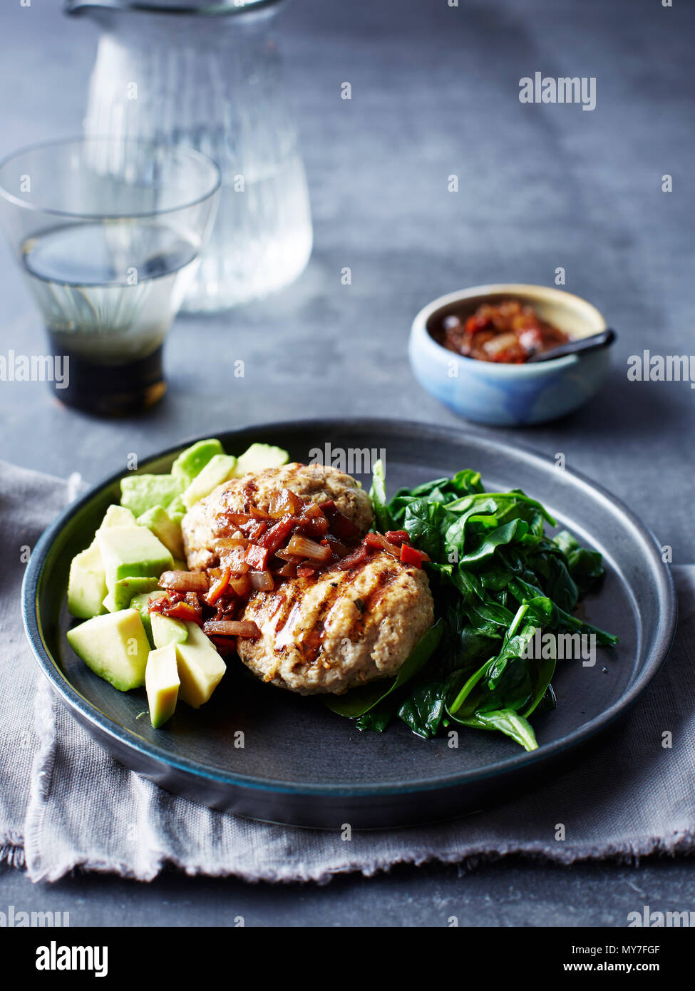 Still life with plate of chicken patty, avocado, onion and chilli jam Stock Photo