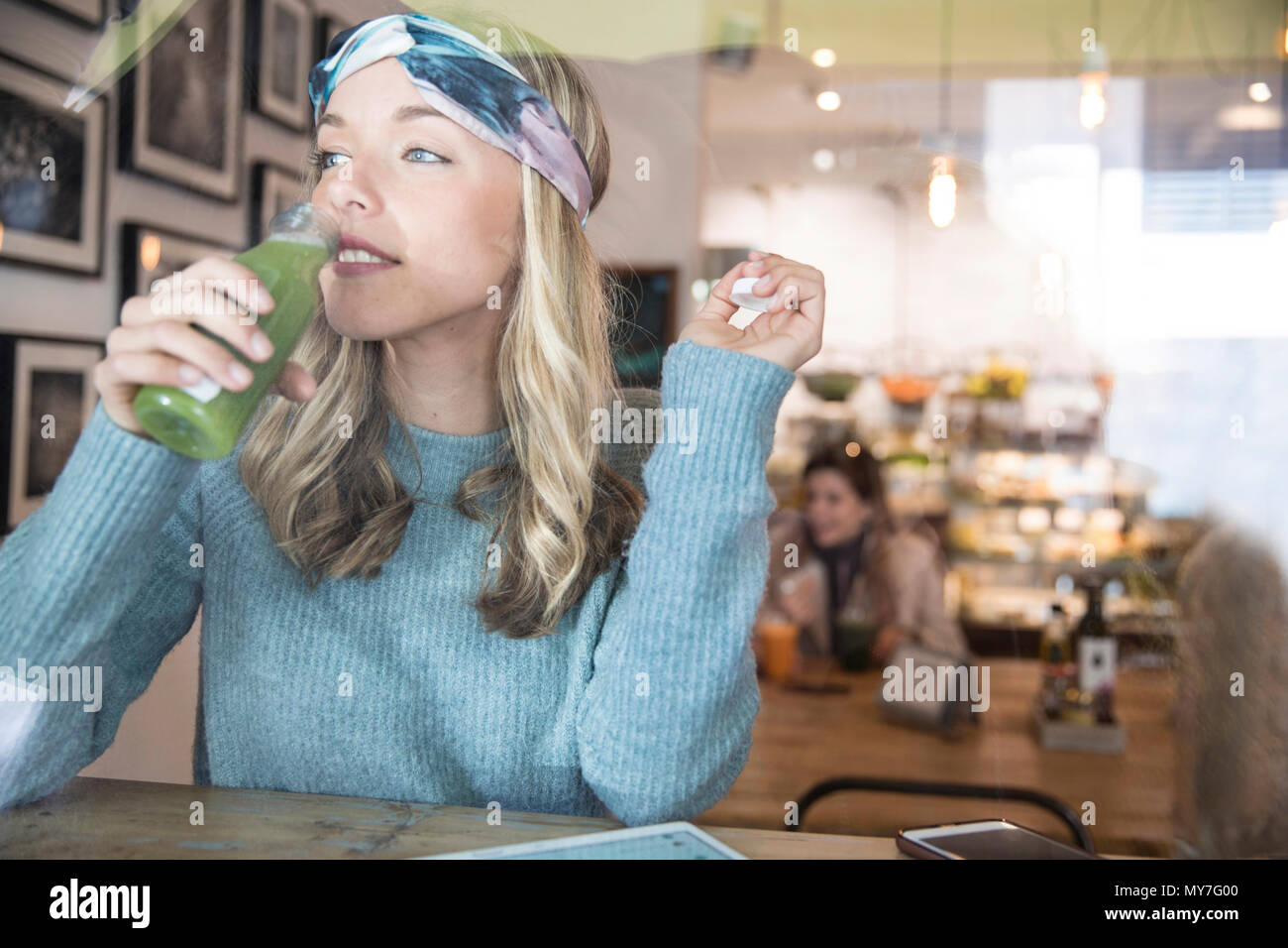 Young woman drinking vegetable juice at cafe window seat Stock Photo