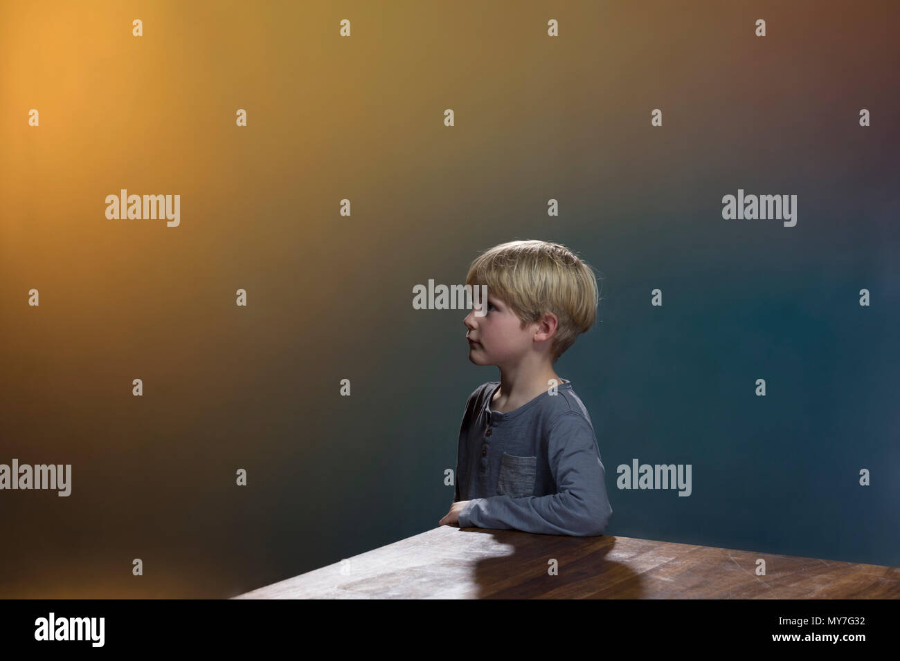 Boy at table, gold and blue background Stock Photo