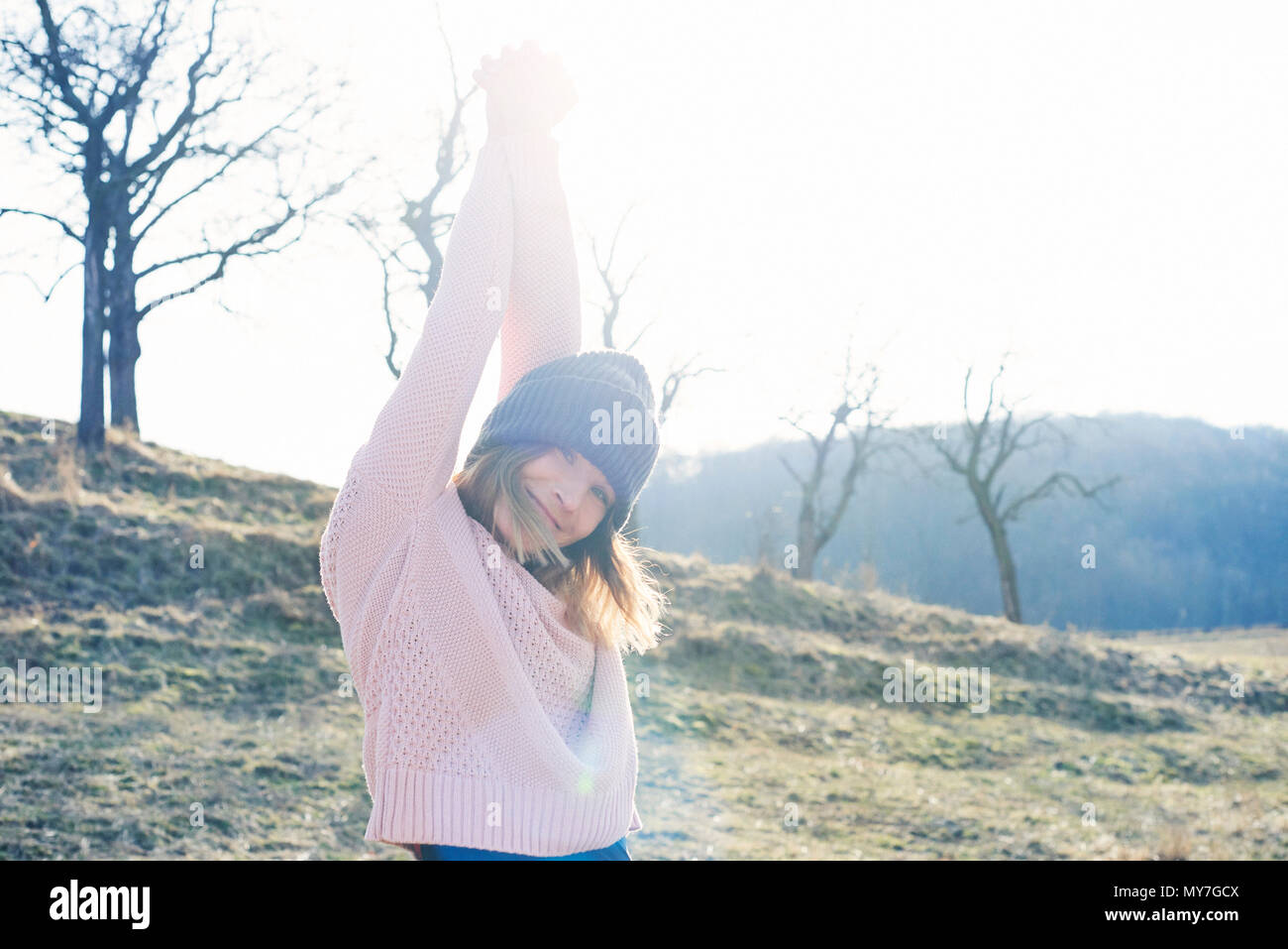 Portrait of mid adult woman with arms raised in sunlit field Stock Photo