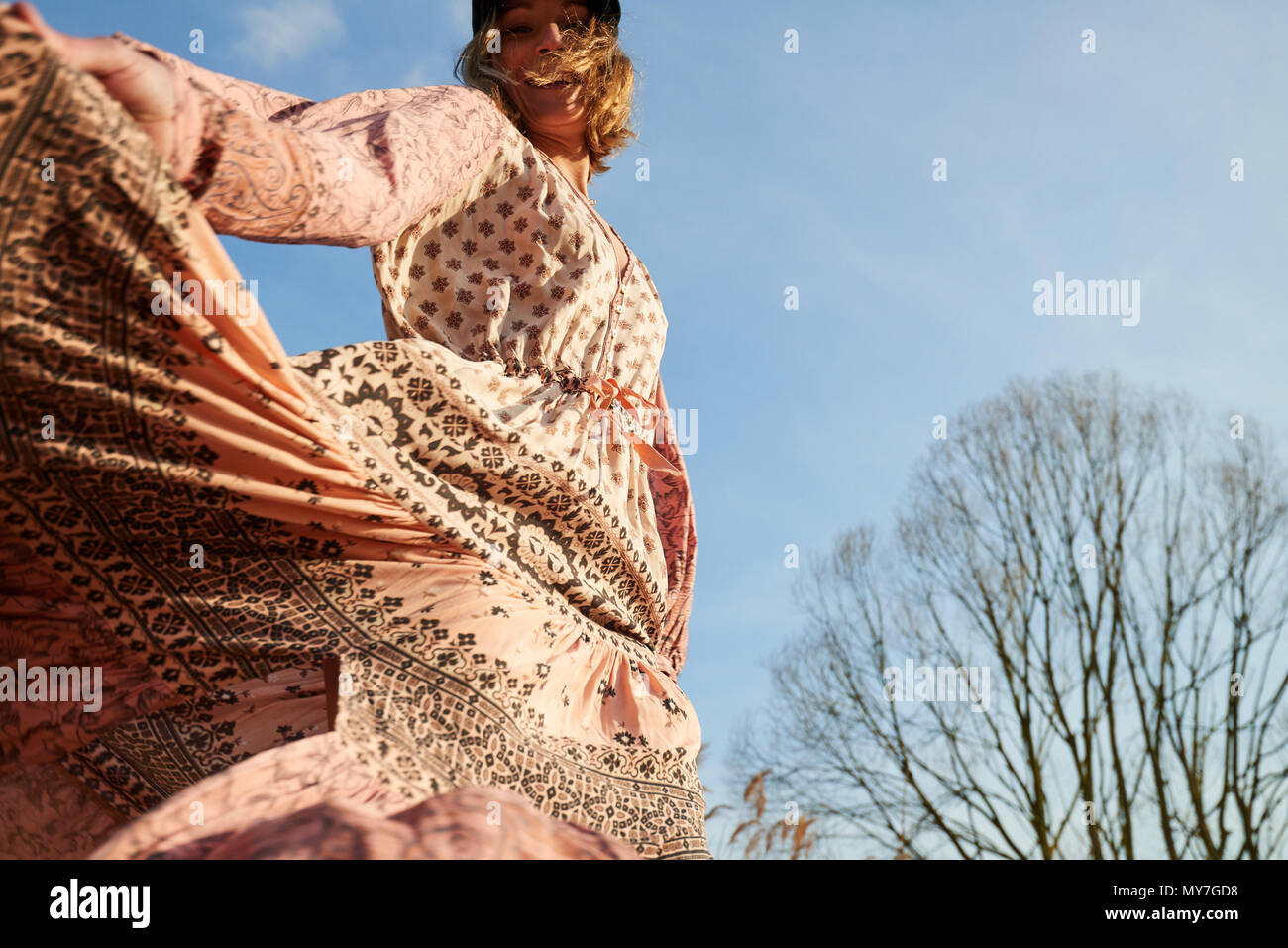 Hippy style woman dancing against blue sky, low angle view Stock Photo