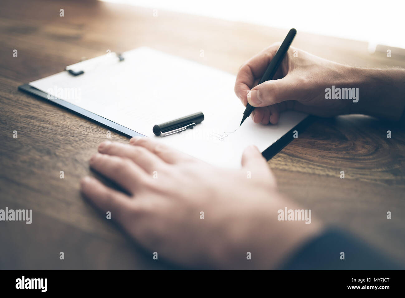 close-up of businessman signing contract or document on wooden desk Stock Photo