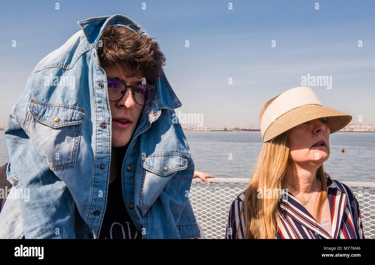 Young man covering his head with a denim jacket, protecting himself from hot sun, Ellis Island ferry, New York City, USA Stock Photo