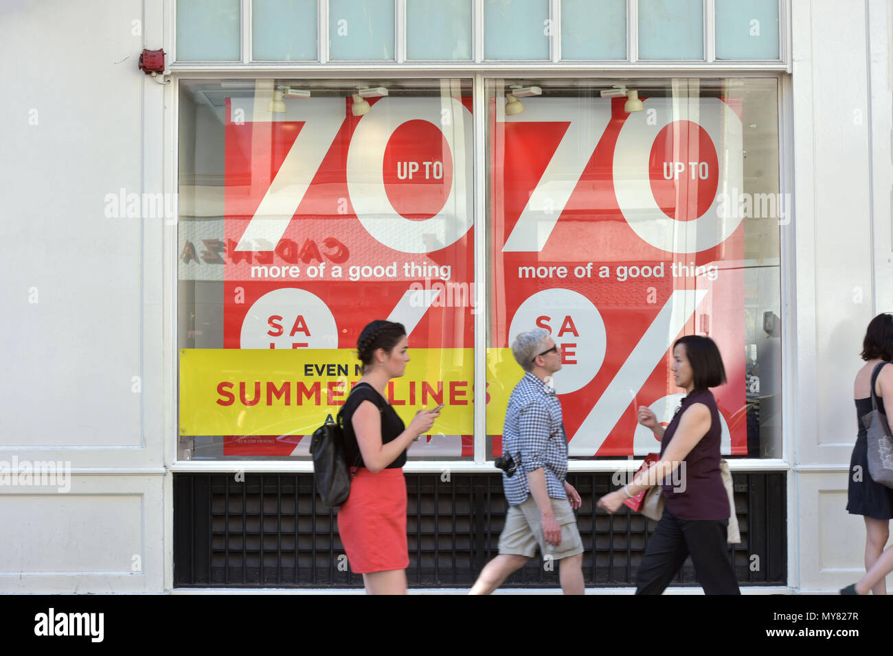Tourists and shoppers walk past the shops with 70% further reduction and summer sale signs, on Long Acre, Covent Garden Stock Photo