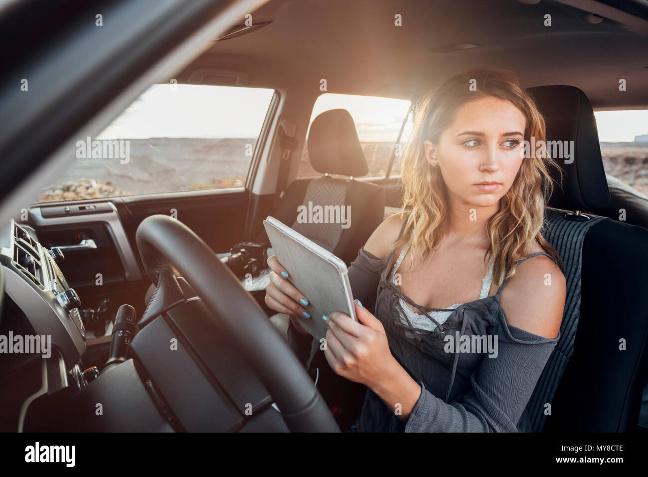 Young woman sitting in vehicle, holding digital tablet, looking out of window, Mexican Hat, Utah, USA Stock Photo