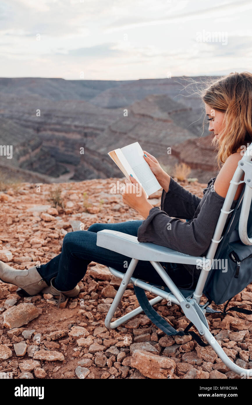 Young woman in remote setting, sitting on camping chair, reading book, Mexican Hat, Utah, USA Stock Photo