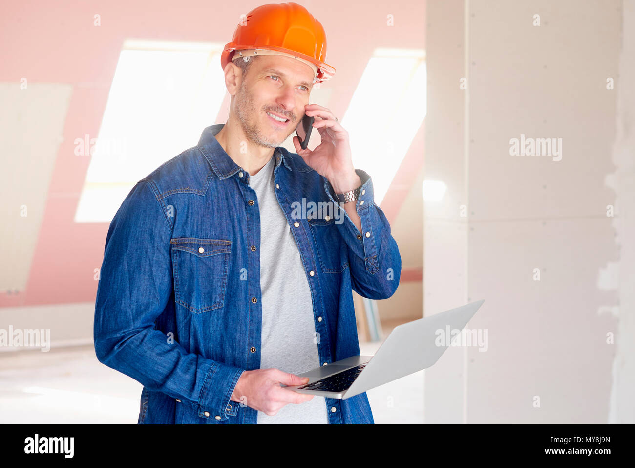 Construction man making call and using his laptop while standing at construction site. Stock Photo