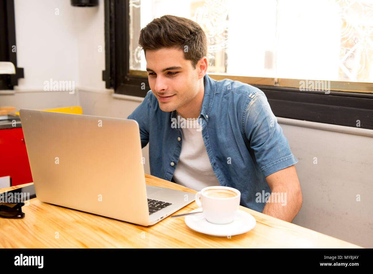 Portrait of a young caucasian man using laptop at a cafe. Causally dressed student working on computer while drinking coffee in education communicatio Stock Photo