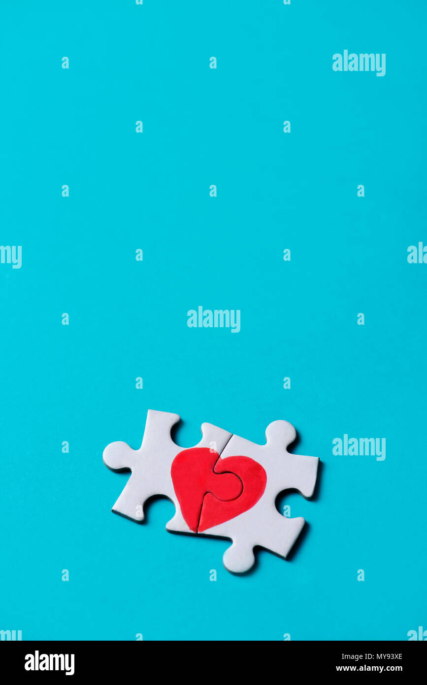 two pieces of a puzzle forming a heart, depicting the idea that love is a matter of two, on a blue background, with some blank space on top Stock Photo