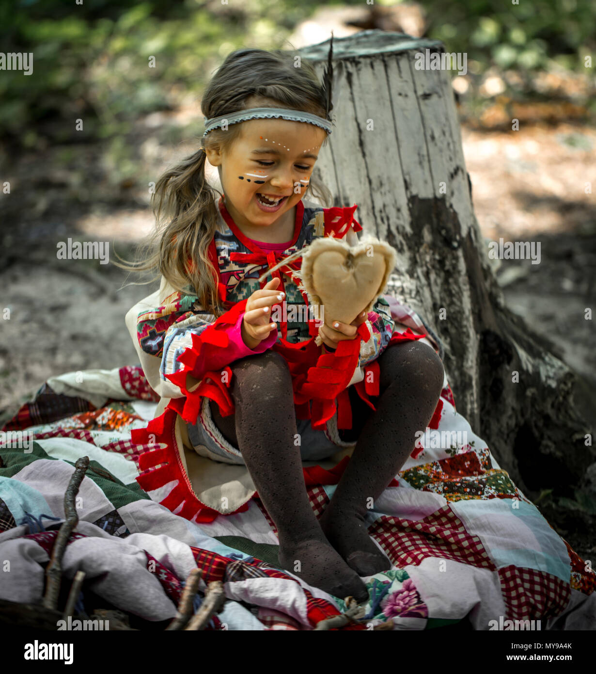 beautiful little girl playing outdoors in Indians ,eating an Apple sitting on a stump Stock Photo