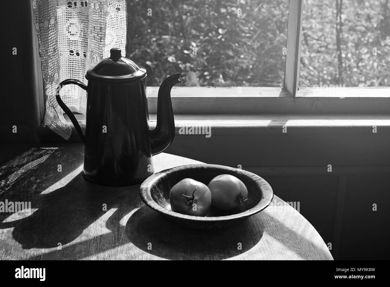 Vintage coffee pot and the two tomato in metallic plate on the round table in the retro interior. Black and white Stock Photo