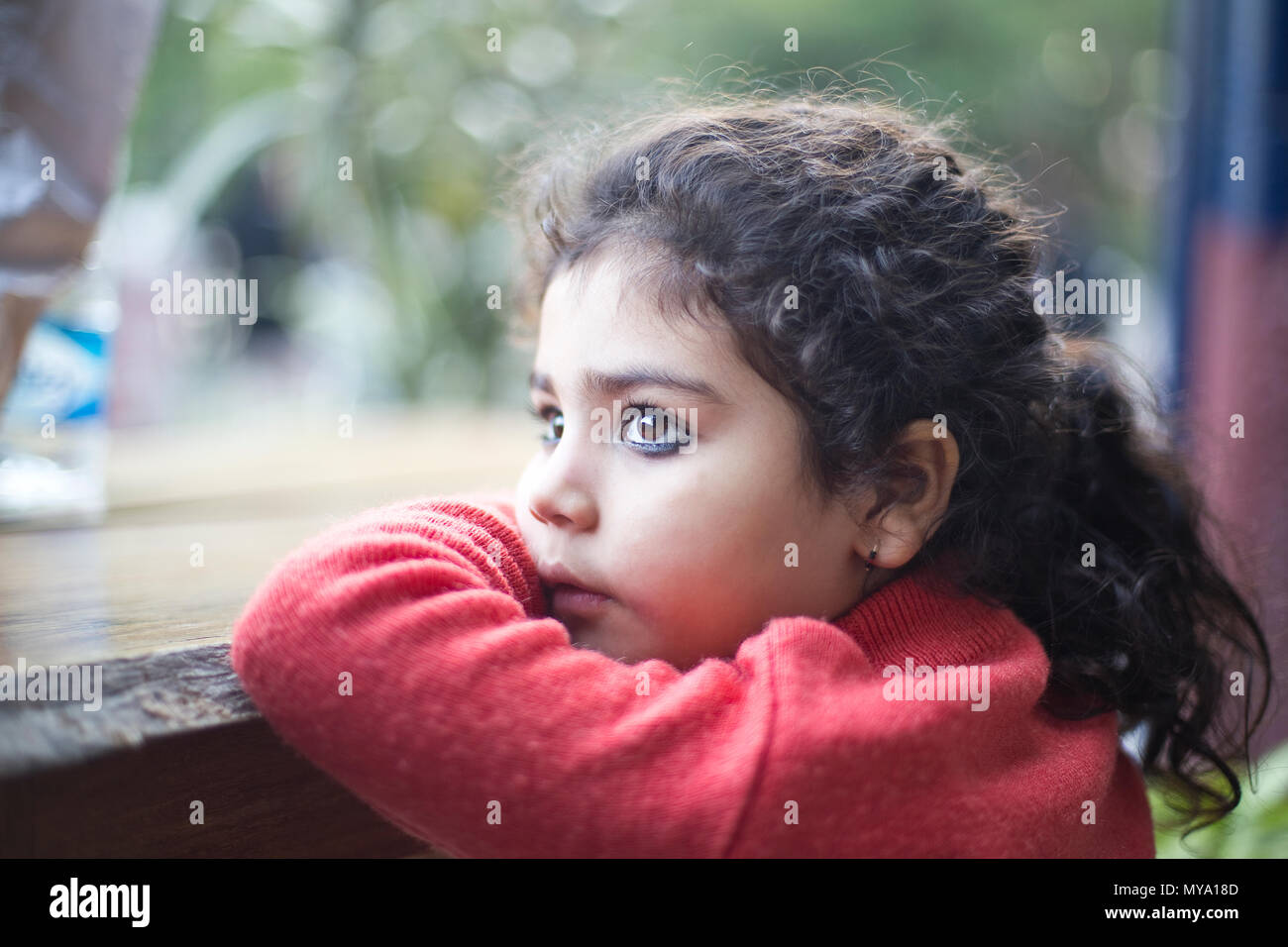 Thoughtful Indian girl looking out through window Stock Photo