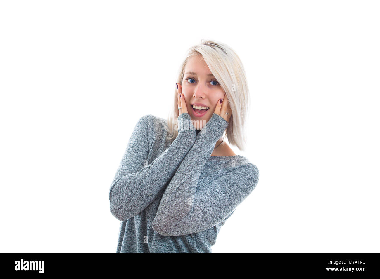 Casual blonde girl positively surprised with hands on her cheek. Beautiful young woman holding her mouth opened, wow shock concept. Stunned human emot Stock Photo