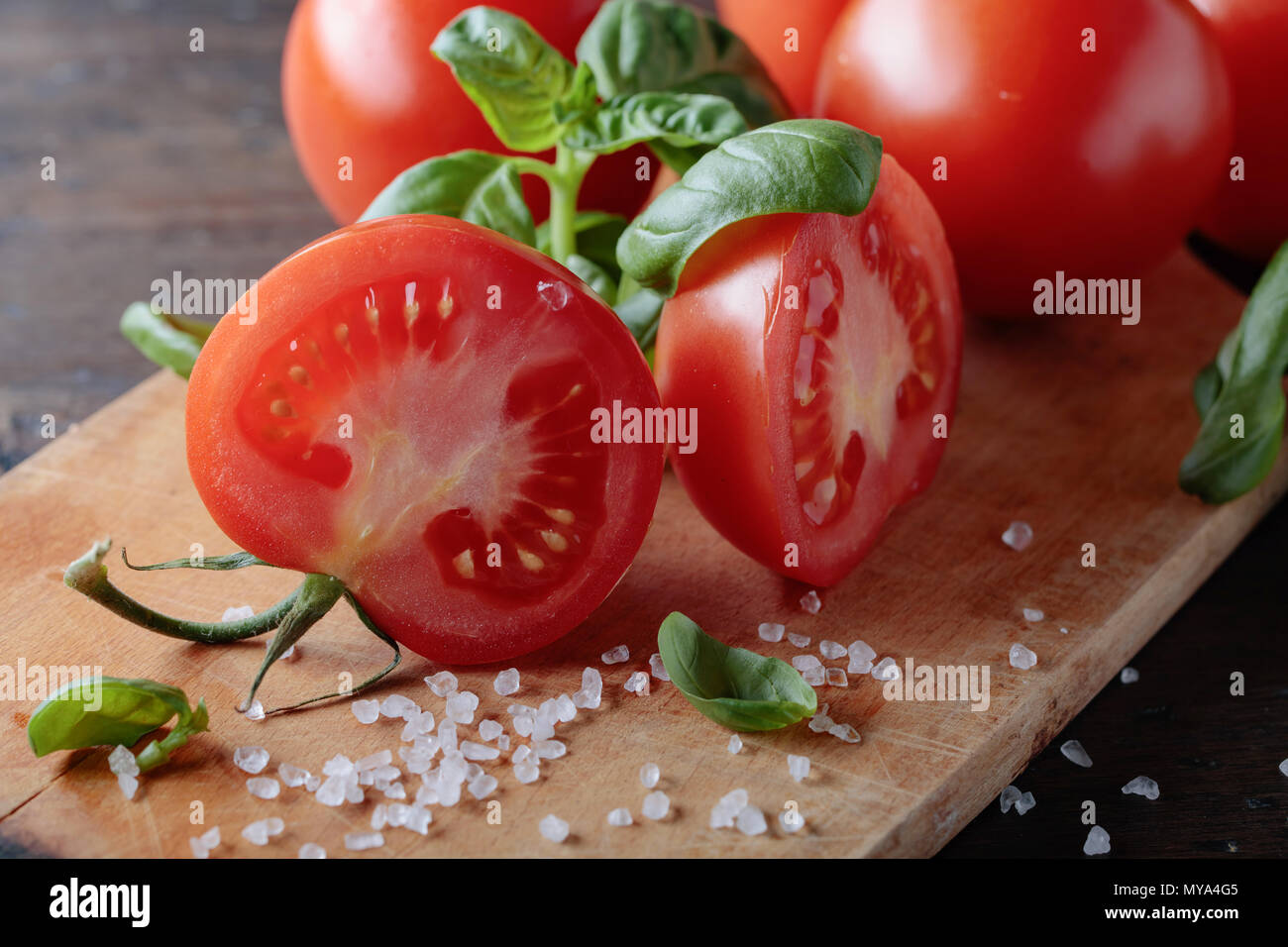Red tomatoes with green basil and sea salt on wooden table background ...