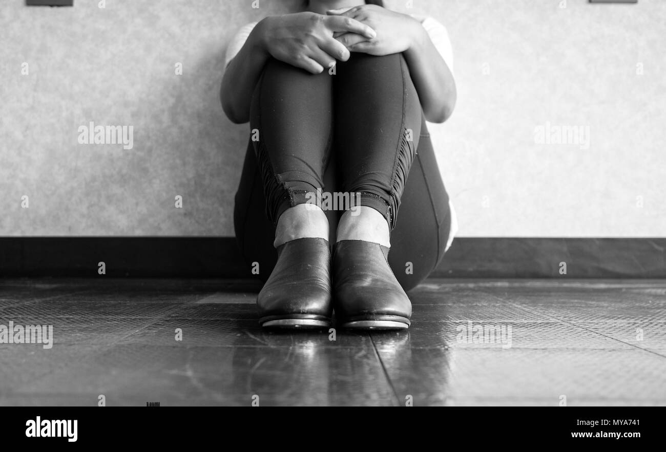 Black and white version of Tap dancer sitting down and holding her legs Stock Photo