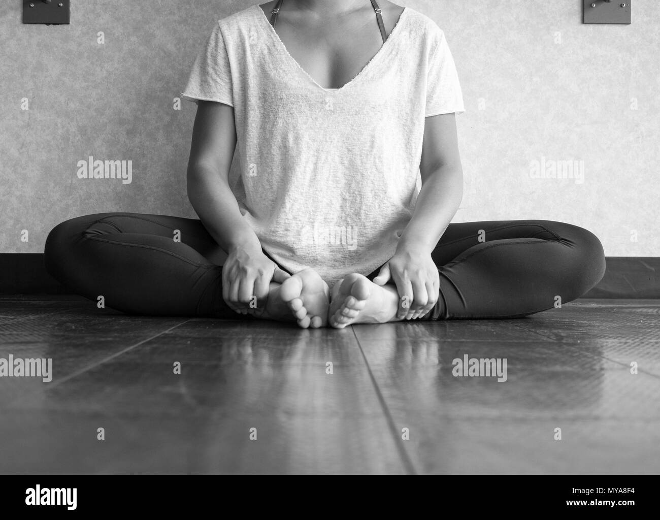 Black and white version of Female dancer sitting down in butterfly pose practicing yoga in the studio Stock Photo