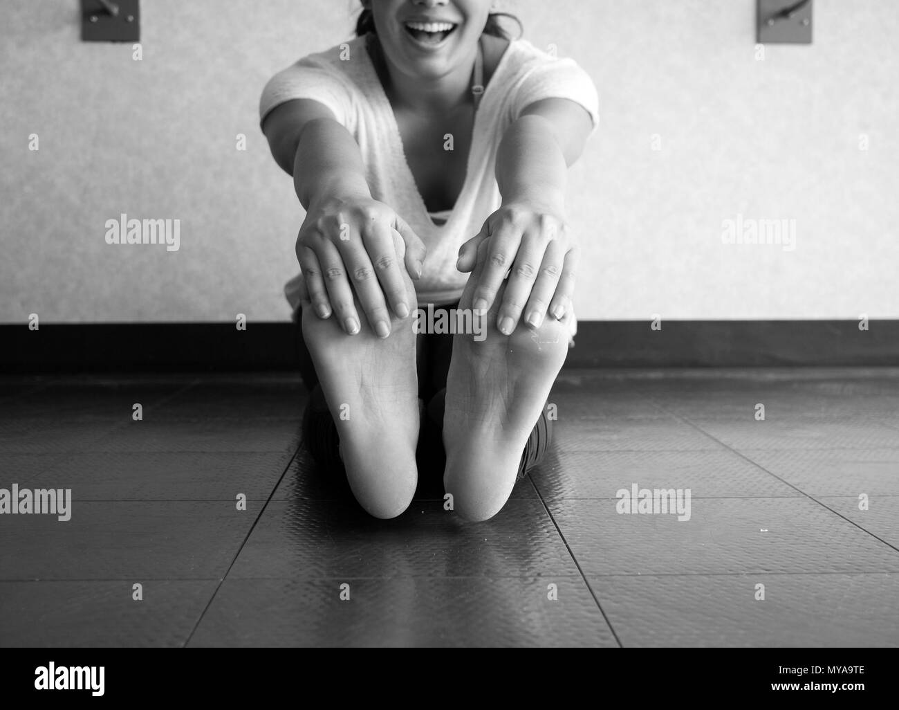 Black and white version of Smiling active woman grabbing her feet to stretch hamstrings in the studio Stock Photo