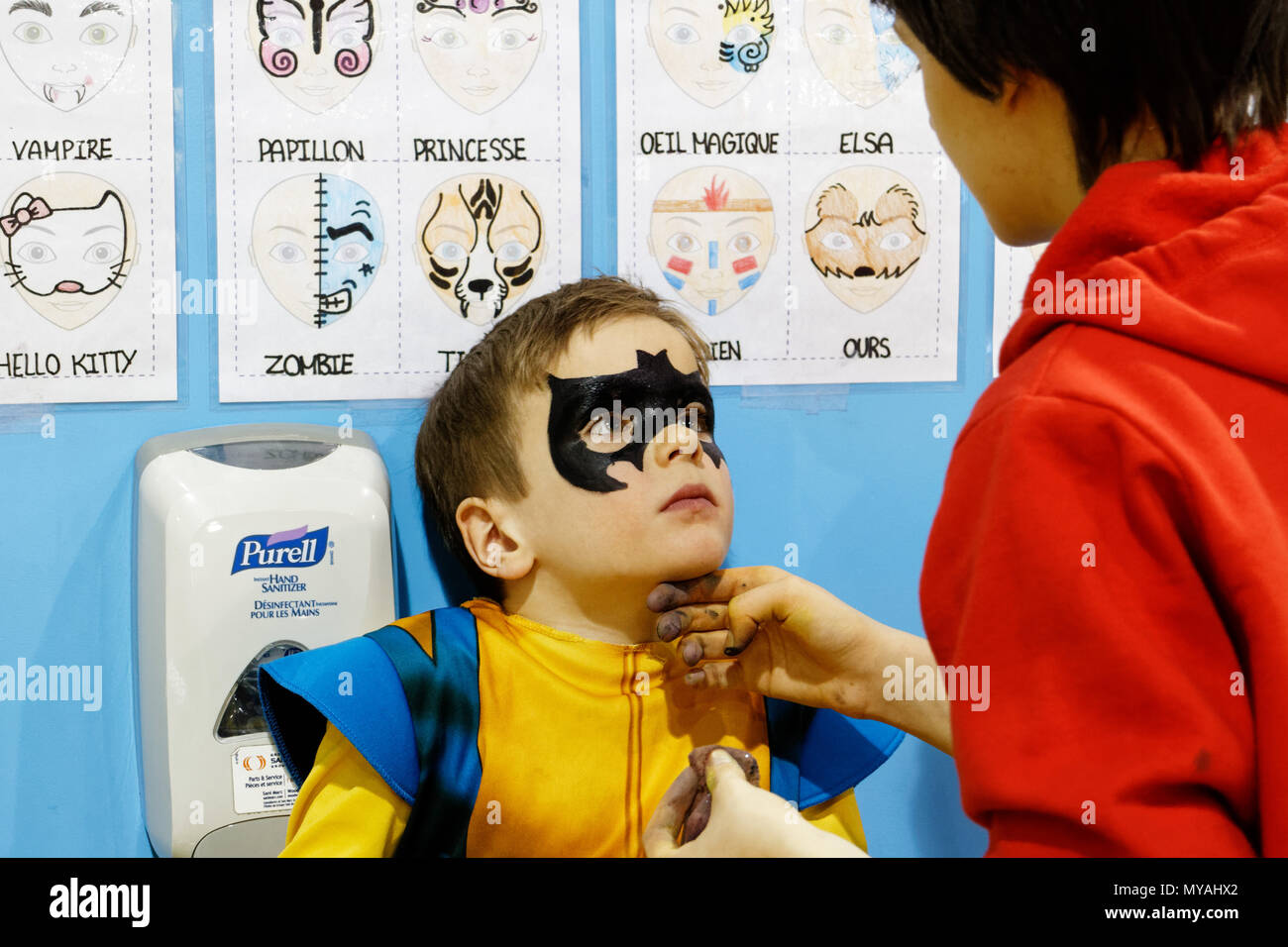 A woman doing a young boy (6 yrs old) face painting as Batman at a children's party Stock Photo