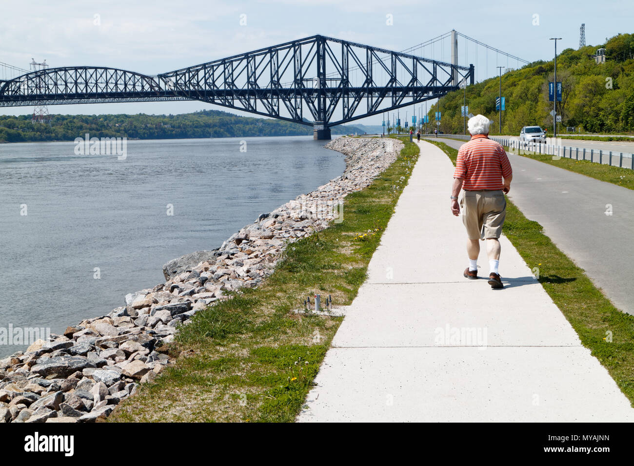 An older man walking on  Promenade Samuel de Champlain park in Quebec City, with the St Lawrence river at Pont du Quebec bridge beyond Stock Photo