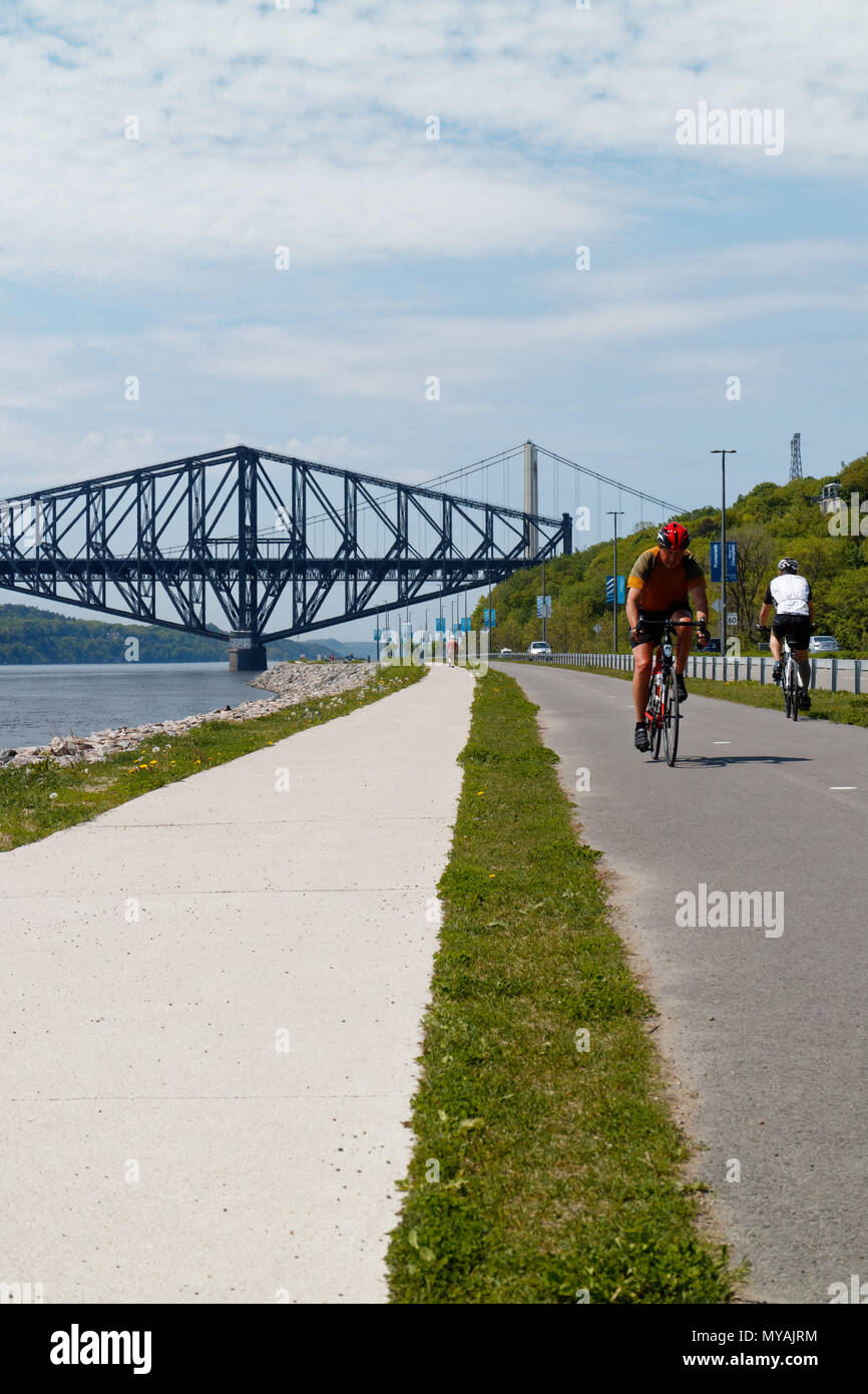 Cyclists on the Promenade Samuel de Champlain bike path in Quebec City, with the St Lawrence river at Pont du Quebec bridge beyond Stock Photo