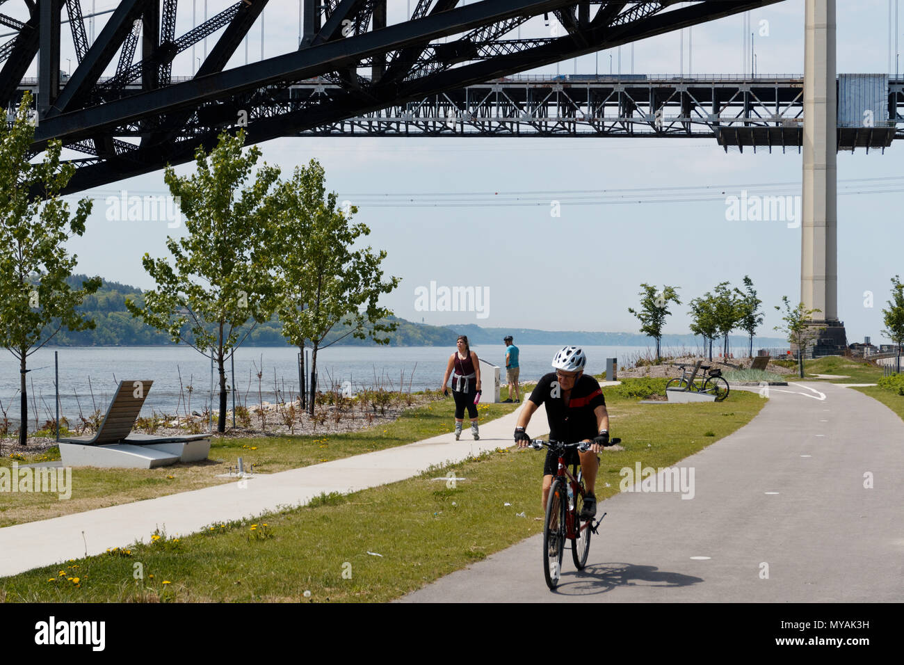 Cyclists on the Promenade Samuel de Champlain bike path in Quebec City, with the St Lawrence river at Pont du Quebec bridge beyond Stock Photo