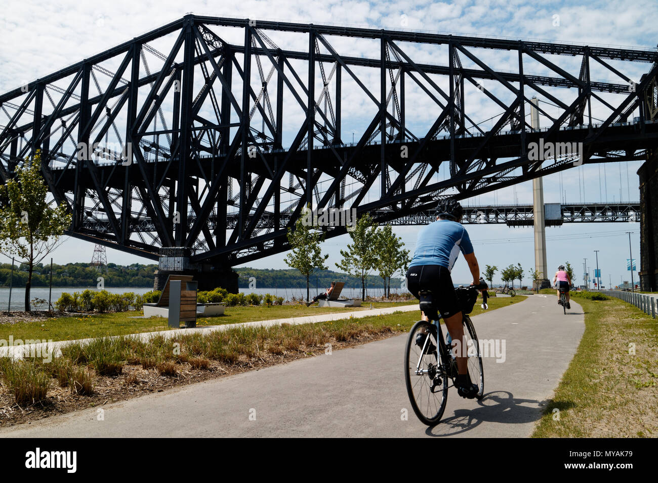 Cyclists on the Promenade Samuel de Champlain bike path in Quebec City, with the St Lawrence river at Pont du Quebec bridge beyond Stock Photo