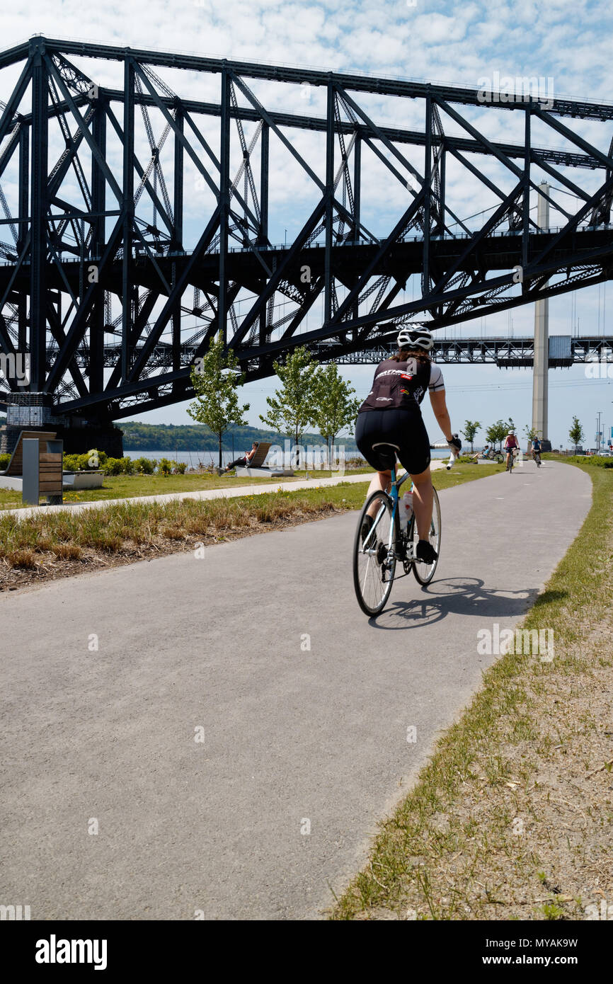 Cyclists on the Promenade Samuel de Champlain bike path in Quebec City, with the St Lawrence river at Pont du Quebec bridge beyond Stock Photo