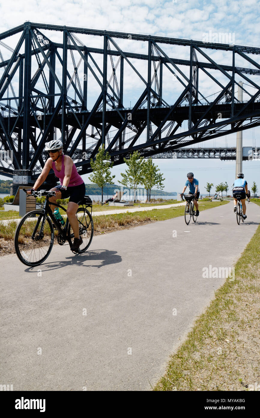 Cyclists on the Promenade Samuel de Champlain bike path in Quebec City, with the St Lawrence river at Pont du Quebec bridge beyond Stock Photo