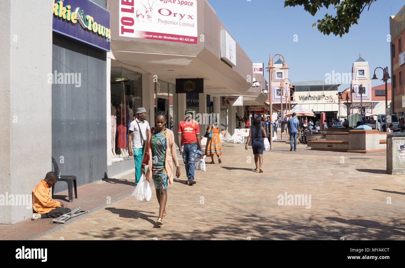 WINDHOEK NAMIBIA - MAY 10 2018; People in African city street walking past shops and beggar Stock Photo