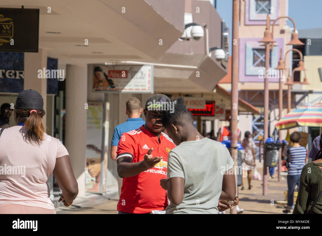 WINDHOEK NAMIBIA - MAY 10 2018; Two young African men in conversation on African city street with others walking by Stock Photo